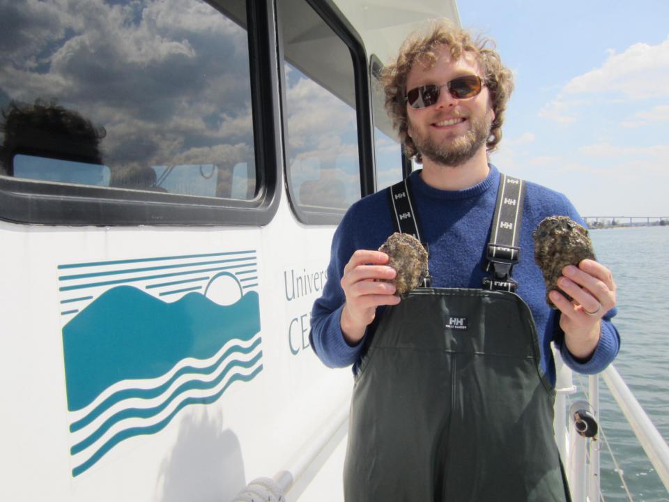 Mike Wilberg stands on deck of Rachel Carson research vessel holding oysters