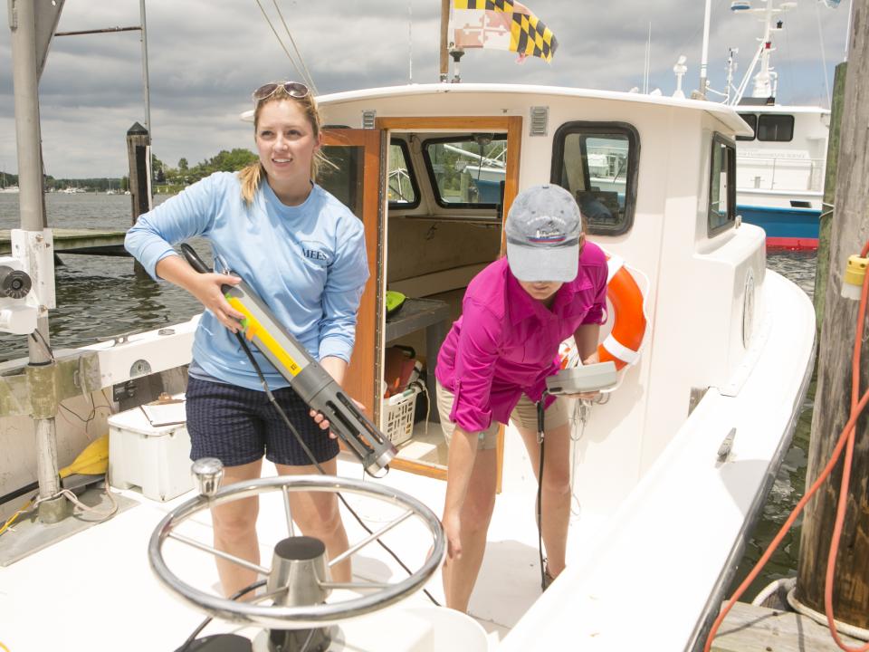 Two students ready on a boat get equipment ready to make water quality measurements