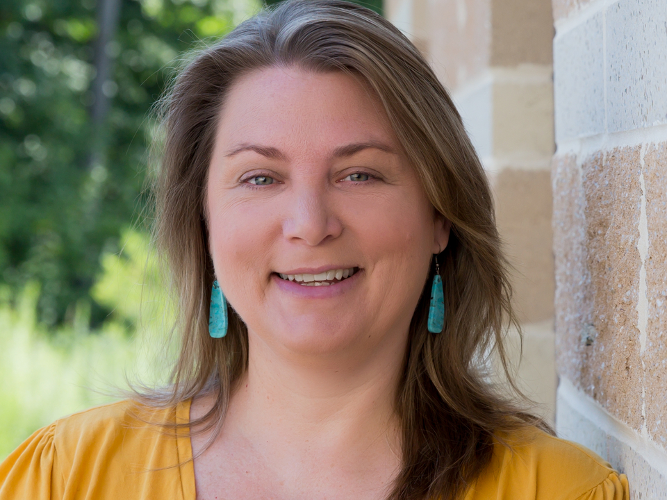 Headshot of Dr. Emily Cohen leaning against a sandstone colored building wearing a dark yellow blouse. 