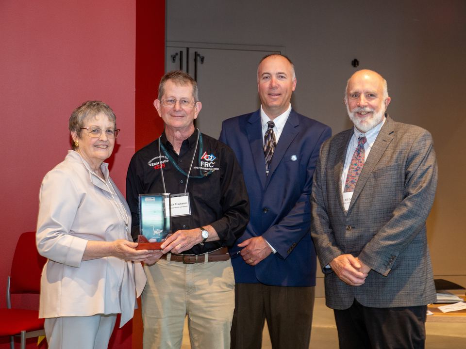 Dr. Brenda McCartney, Chuck Trautwein, Dr. David Nelson and Dr. Bill Dennison pictured with Inspiration Award trophy with red wall in background. 