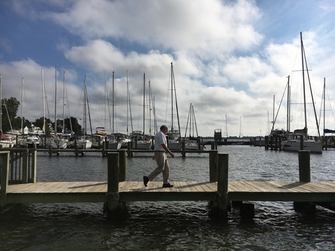 A man walks along a pier in a Annapolis with sailboats behind him.