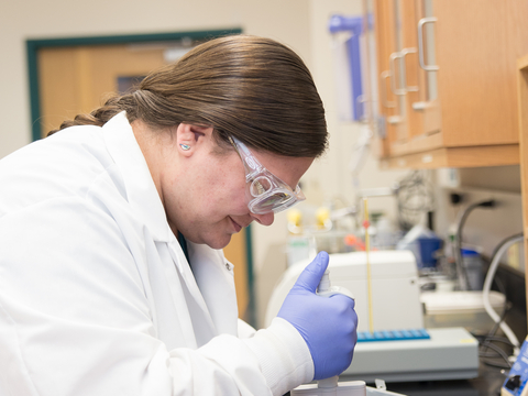 Graduate student Juliet Nagel in lab coat, goggles and gloves in laboratory. 