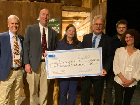 From left to right: Dr. Peter Goodwin, Dr. David Nelson, Janice Keene holding large prop check, Francis "Champ" Zumbrun, Adron Fiscus, and Marta Fiscus. All are standing in barn, facing camera. 