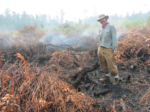 Mark Cochrane stands in a peat field that's smoldering from a wildfire.