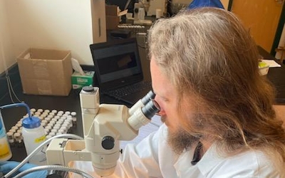 Intern Richard Johnson, wearing white lab coat, examines samples under a microscope. 