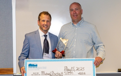 Mick Burkett and David Nelson holding inspiration award and ceremonial check with white marker board in background. 