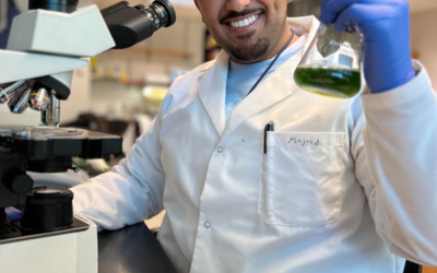 Majeed in the lab, holding up a beaker with algae