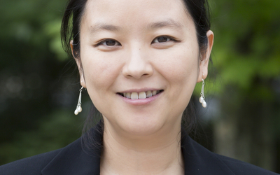 Head shot of Xin Zhang with green leaves in background. 