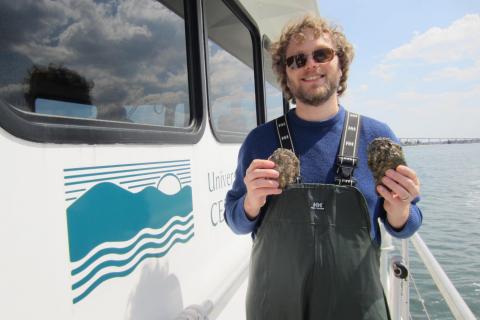 Mike Wilberg stands on deck of Rachel Carson research vessel holding oysters