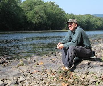 Photo of Tom Mathews seated next to a river.