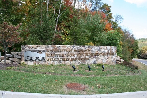 Grey stone UMCES sign at entrance to Appalachian Laboratory. Green grass in the foreground with trees just changing to orange in the back. 