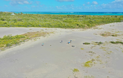a drone photo shows a tropical island, Anegada, from above with small figures pictured standing beside one of the stranded coral boulders on the beach.