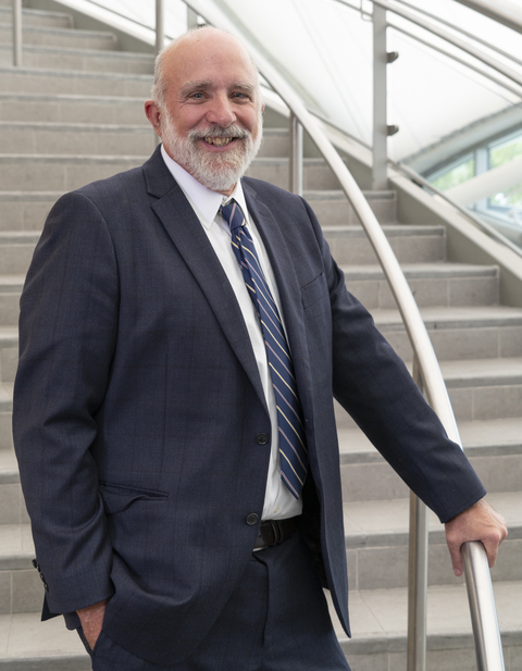 Bill Dennison dressed in blue suit stands on stairs with hand on railing