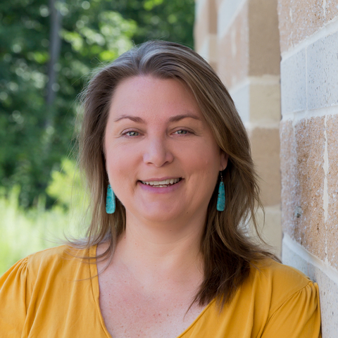 Headshot of Dr. Emily Cohen leaning against a sandstone colored building wearing a dark yellow blouse. 