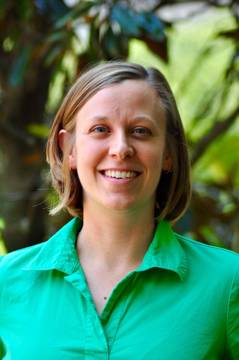 Headshot of Megan Fritz in green short with blurred green plants in background. 