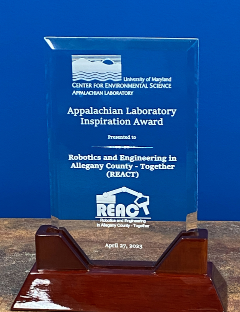 Clear Inspiration Award plaque with wooden base against UMCES blue background