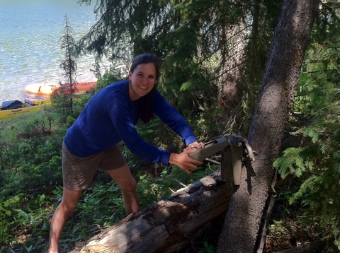 Kelly Pearce attaching a camera to a tree with lake in background. 