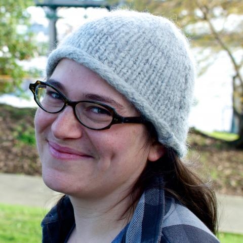 Headshot of smiling Dr. Clara Fuchsman wearing grey knit hat and eyeglasses