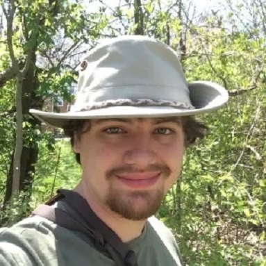 Headshot of Cody Kent in forest wearing grey hat and green t-shirt. 