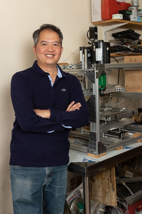 Dung Minh Hoang in foreground, standing with arms crossed, with equipment in background. 
