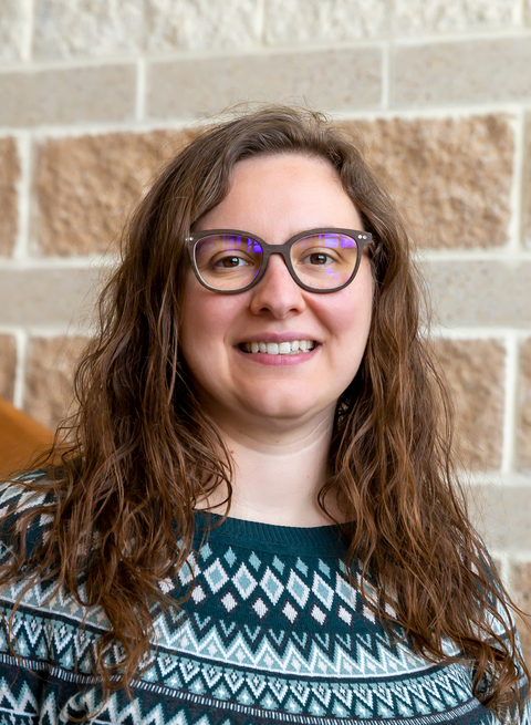 Headshot of Marie Pegard in blue and white sweater standing before a red/white brick wall. 