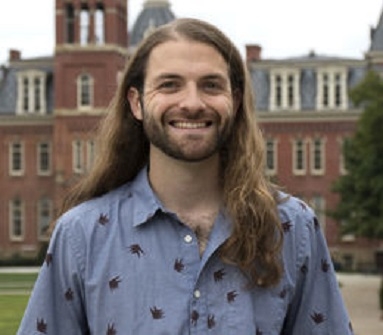 Headshot of Justin Mathias in front of academic building. 