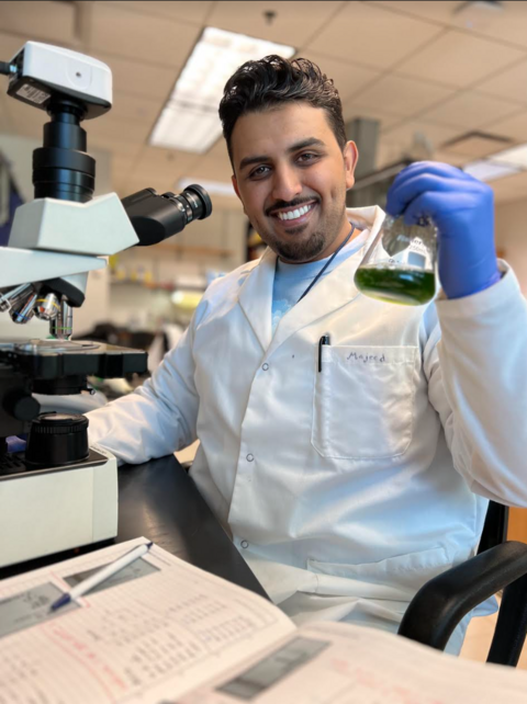 Majeed in the lab, holding up a beaker with algae