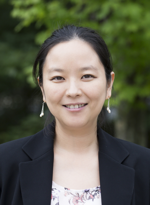 Head shot of Xin Zhang with green leaves in background. 