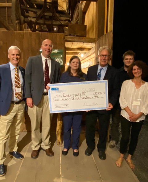 From left to right: Dr. Peter Goodwin, Dr. David Nelson, Janice Keene holding large prop check, Francis "Champ" Zumbrun, Adron Fiscus, and Marta Fiscus. All are standing in barn, facing camera. 