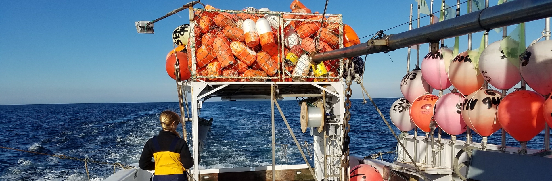The bow of a research vessel filled with buoys and the wake of the boat.