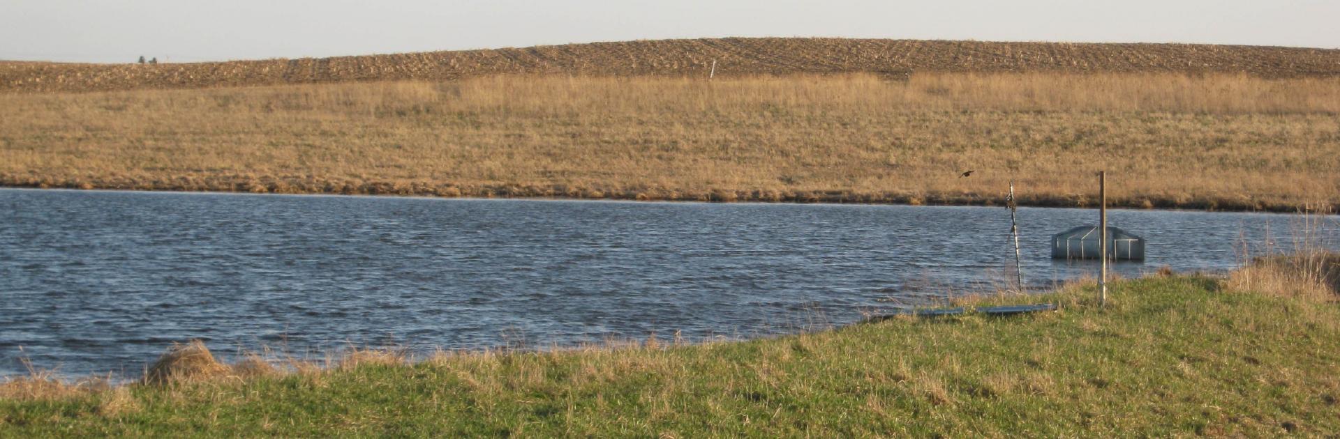 A marshy landscape with a waterway cutting through the center under a blue sky.