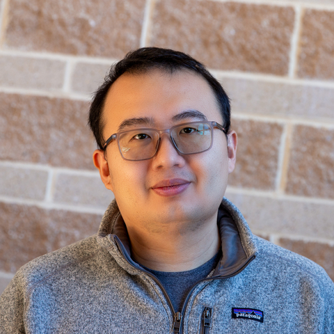 Head and shoulders photograph of Yuhao Wang standing in front of a stone wall
