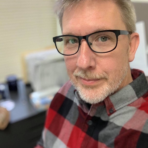 Picture of Kevin Bruce looking into camera, wearing a flannel shirt and a slightly too-smug look on his face, denoting the coder-side of his position.