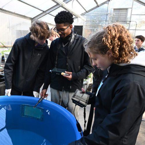 Three students stand over a large tank of water to take water quality measurements