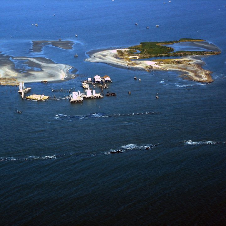 Aerial photo showing land loss inshore of protection barriers and subsequent flooding of facilities