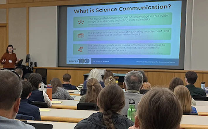 Science Communication presentation on screen with spectators looking on