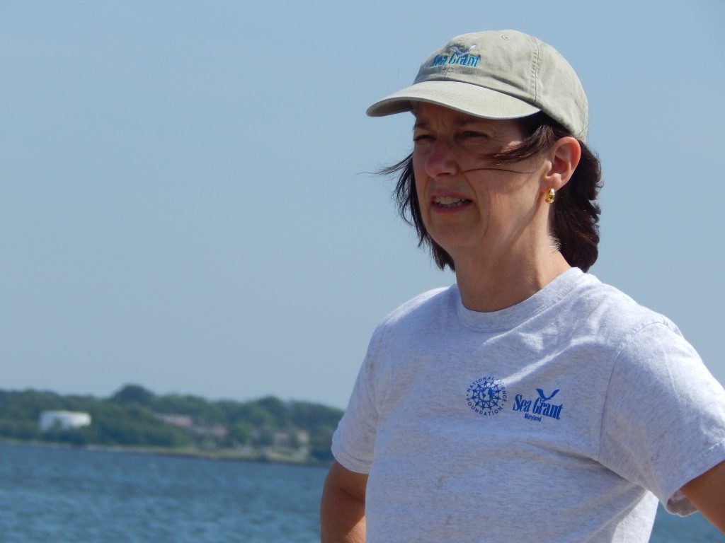 Fredrika Moser in a baseball cap and Sea Grant T-shirt stands near a body of water