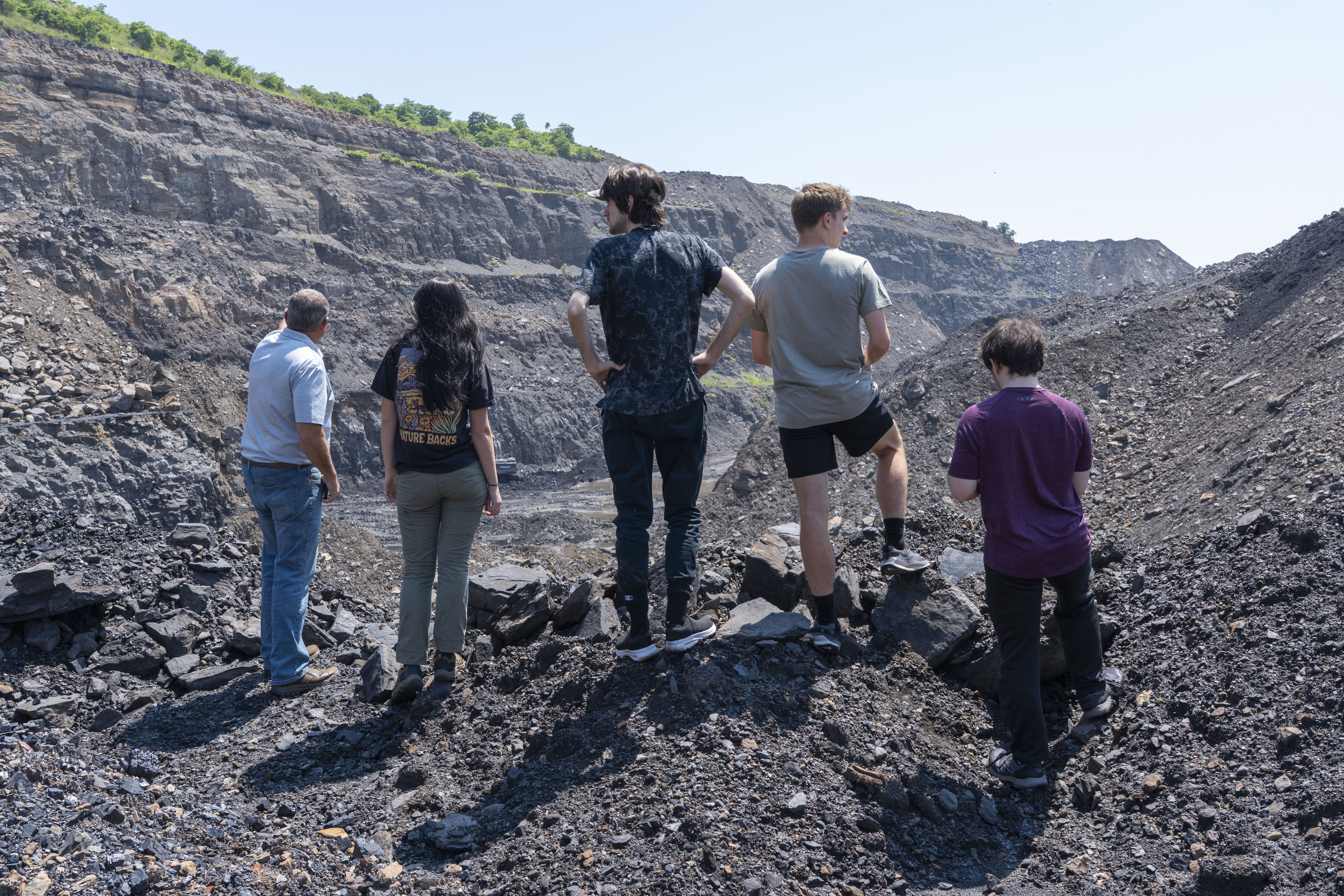 Interns facing away from camera, standing on large pile of coal, surveying an abandoned coal mine.