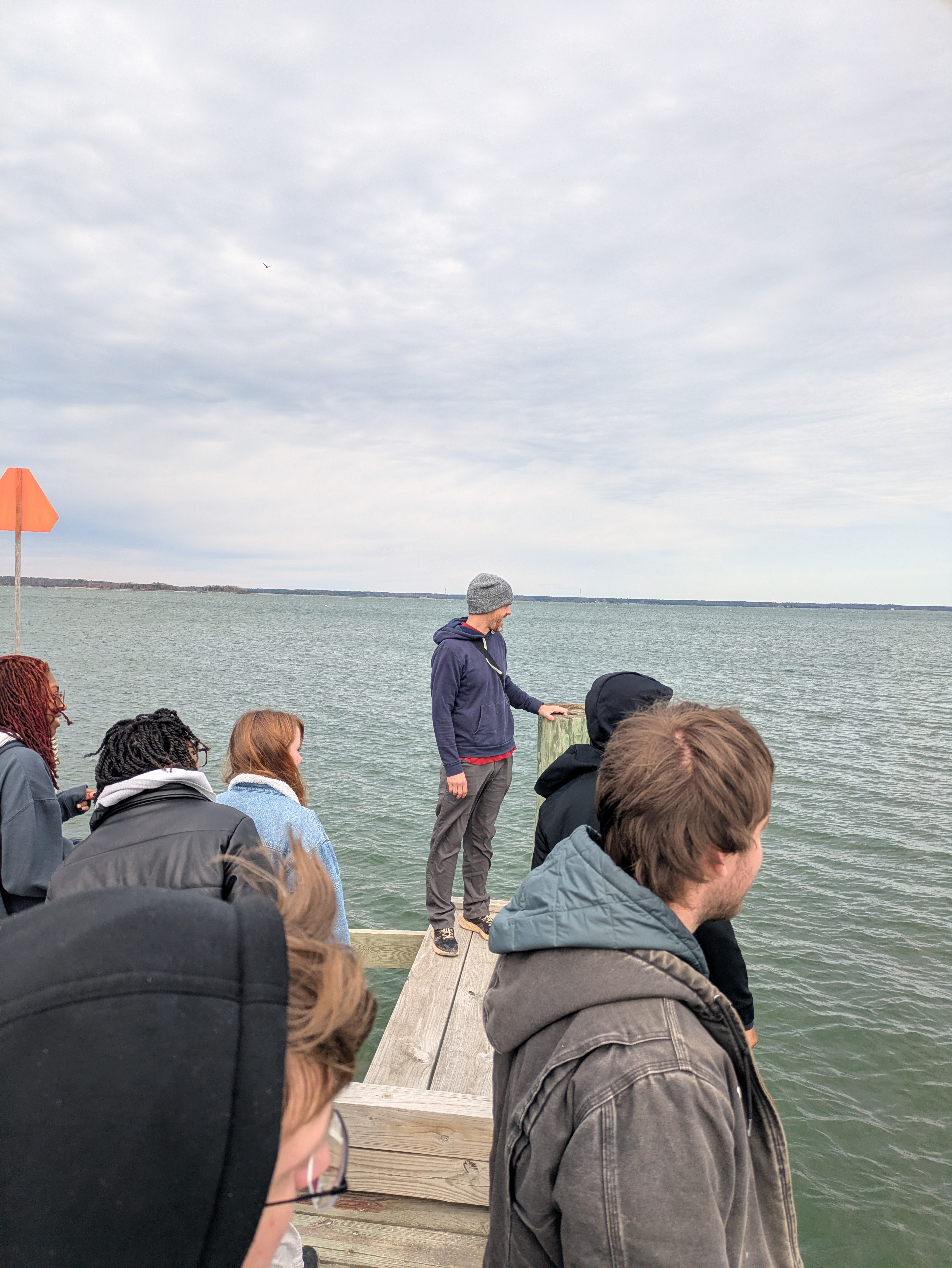 Several individuals gather on a dock, looking out at something unseen on the water.